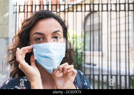 Young woman putting on a surgical mask in the street to protect herself and take hygienic safety measures. Concept of protection and safety Stock Photo