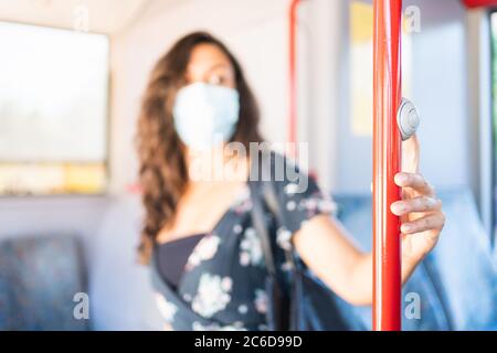 Young woman looking at the driver with a protective mask touching the stop button to get off the bus. Protective concept Stock Photo