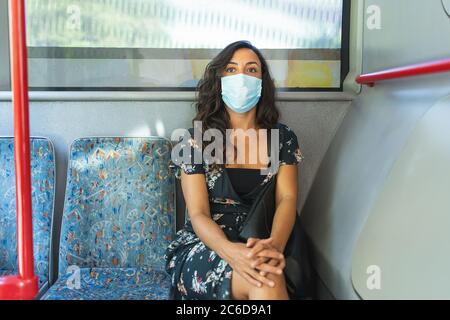 A young woman in a dress with black hair wears a protective mask on her face while sitting on a public bus. Concept of security. Stock Photo