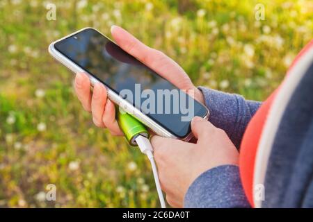 A girl uses a smartphone outdoors while charging from an external power bank Stock Photo