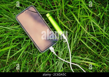 Smartphone and external power bank lie on green grass in the park while charging Stock Photo