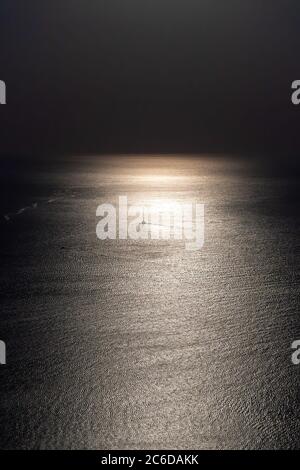 Silhouette of the yacht or leisure boat sailing toward the moon. Dark sky and Moonwalk. Reflection in water. Beautiful seascape in the night. Harmony Stock Photo