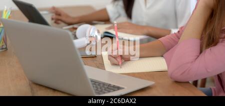 Cropped shot of university students doing their project together with digital devices and stationery on wooden table Stock Photo