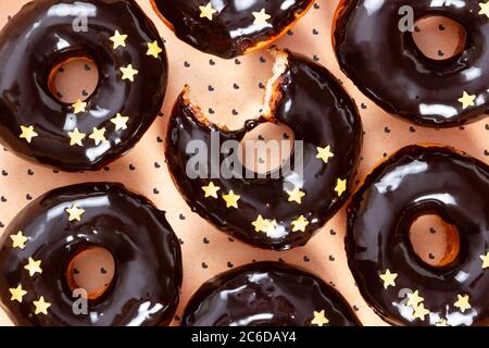 Donuts with chocolate mirror icing and sprinkles on orange background with hearts. Top view. Stock Photo