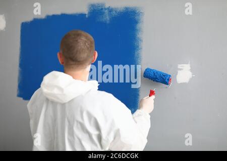 Man with roller in his hands paints wall in blue. Stock Photo