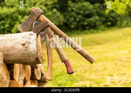 Old rusty axes stuck in a pine block. Lumberjack tools. Work in forest. Preparation of wood for heating. Stock Photo