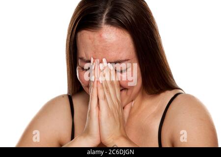 A young happy and shy woman covers her face with her hands on white background Stock Photo