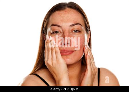 beautiful middle-aged woman applying moisturizer on her face on white background Stock Photo