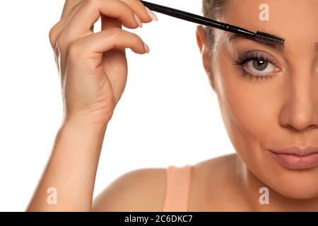 Young woman contouring her eyebrows with dry brush on white background Stock Photo