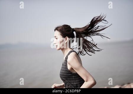 young asian adult woman running jogging outdoors by the sea