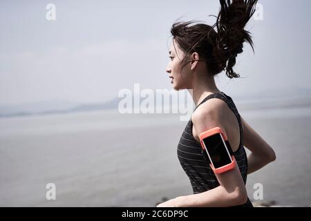 young asian adult woman running jogging outdoors by the sea, side view