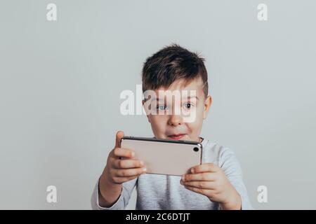 Closeup portrait of a boy who looks into the phone and shows emotions. The boy takes a selfie on the phone Stock Photo
