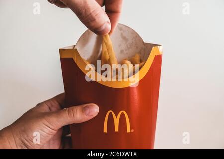 Lviv / Ukraine - April 2020: Close up view of hungry man's hand taking a piece of french fries from Mcdonalds bag. Ordering unhealthy takeaway food Stock Photo