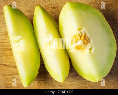 A quarter fresh galia melon with seeds and two slices on a wooden chopping board Stock Photo