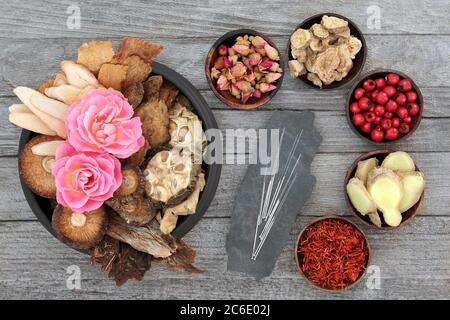 Chinese herbs, fruit and flowers & acupuncture needles used in traditional herbal medicine on rustic wood background. Natural alternative medicine. Stock Photo