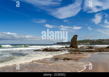 CULLEN BAY BEACH AND TOWN MORAY COAST SCOTLAND A BLUE SKY AND A SANDY BEACH WITH WAVES BREAKING ONTO THE SEA STACK Stock Photo