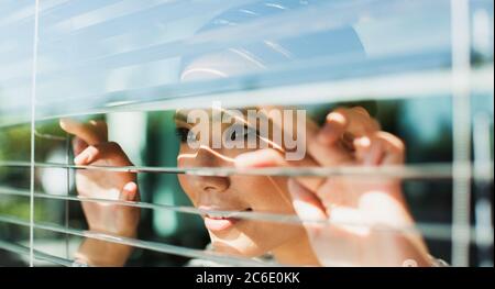 Businesswoman peering through window blinds Stock Photo