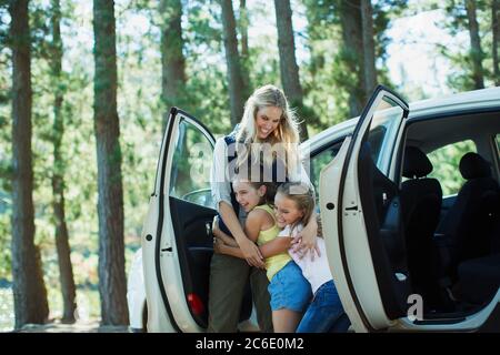 Mother hugging daughters outside car in woods Stock Photo