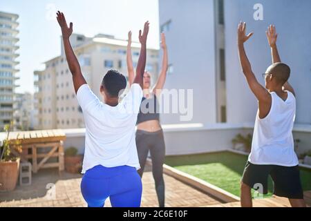 Friends practicing yoga on sunny urban rooftop Stock Photo