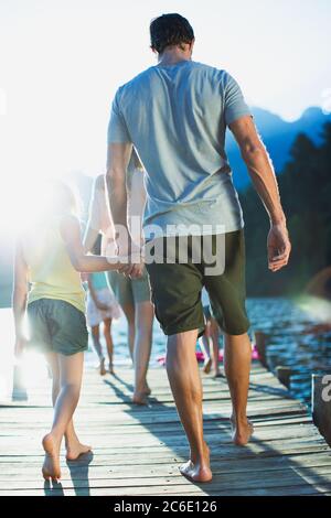 Father and daughter holding hands walking on dock over lake Stock Photo