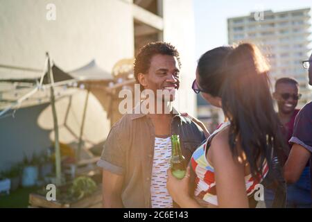 Happy young couple drinking beer on sunny urban rooftop Stock Photo