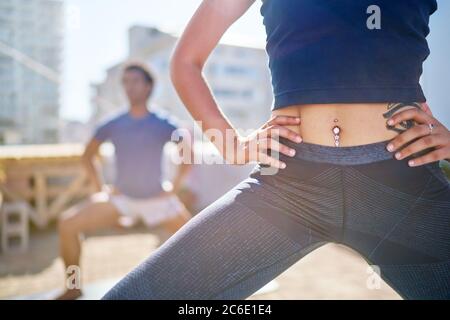 Close up young woman with belly piercing practicing yoga on balcony