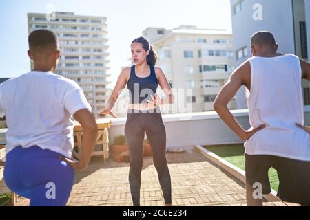 Young female yoga instructor teaching class on sunny urban rooftop Stock Photo