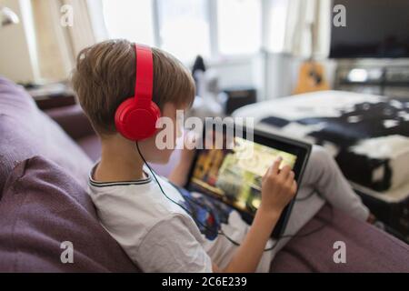 Boy with headphones and digital tablet playing video game on sofa Stock Photo