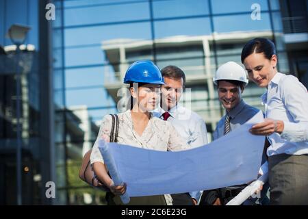 Architects reviewing blueprints outside highrise Stock Photo