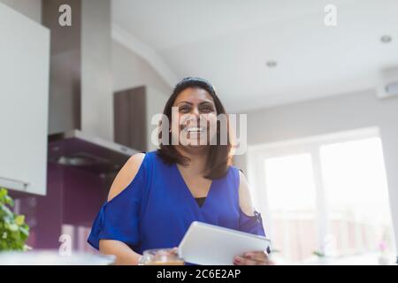 Portrait happy woman using digital tablet in kitchen Stock Photo