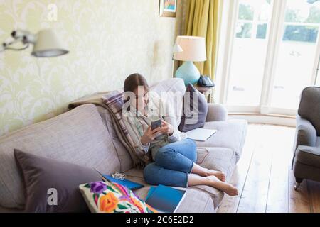 Teenage girl using smart phone on living room sofa