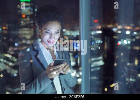 Businesswoman text messaging in urban window at night Stock Photo