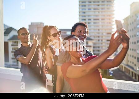 Young friends using smart phone on sunny urban rooftop balcony Stock Photo