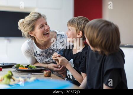 Happy mother and sons eating dinner at table Stock Photo