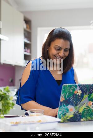 Smiling woman using laptop in kitchen Stock Photo