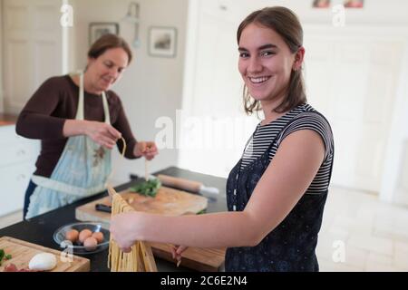 Portrait happy teenage girl making homemade pasta with mother at home Stock Photo