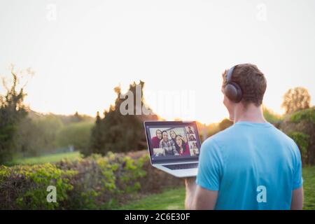 Man with headphones video chatting with friends in sunny garden Stock Photo