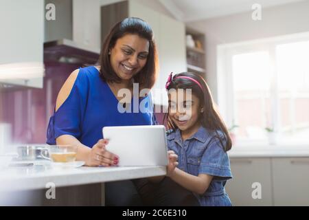 Happy mother and daughter using digital tablet in kitchen Stock Photo