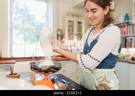 Teenage girl measuring flour for baking in kitchen Stock Photo