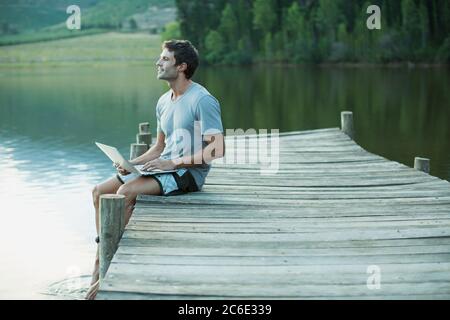 Man using laptop on dock over lake Stock Photo