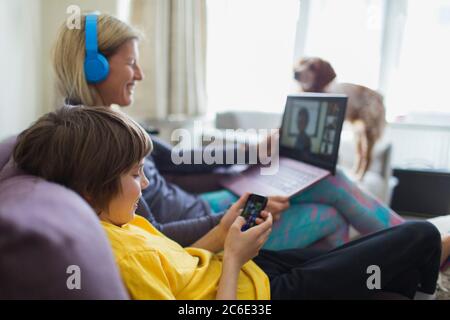 Mother and son using laptop and smart phone on sofa