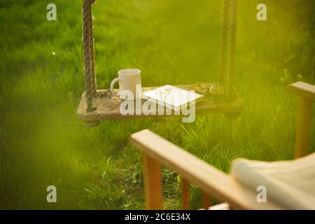Coffee and book on swing in idyllic garden Stock Photo