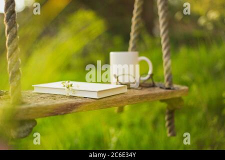 Book coffee and eyeglasses on rustic swing Stock Photo