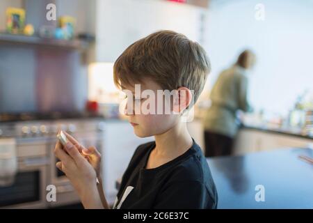 Boy using smart phone in kitchen Stock Photo