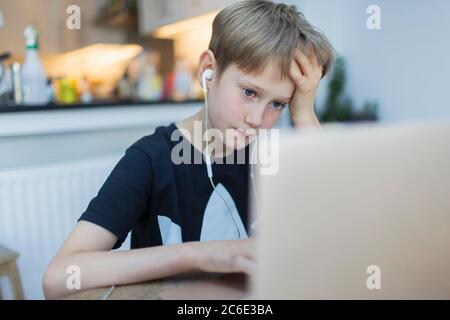 Focused boy with headphones using laptop in kitchen Stock Photo