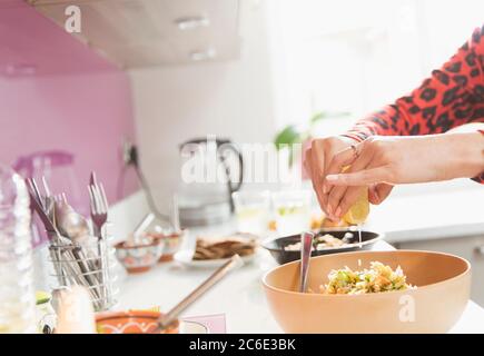 Woman squeezing lemon over bowl of food in kitchen Stock Photo