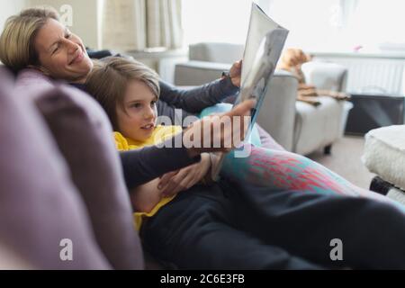 Happy mother and son reading book on living room sofa Stock Photo