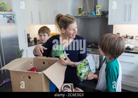 Mother and sons unloading fresh produce from box in kitchen Stock Photo