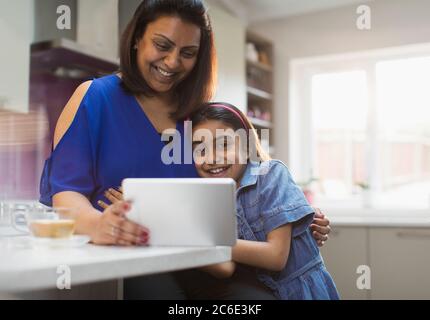 Smiling mother and daughter using digital tablet in kitchen Stock Photo