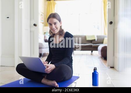 Portrait smiling teenage girl practicing online yoga with laptop at home Stock Photo